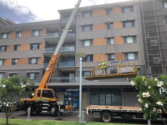 Crane lifting tree limbs away from a multi-storey Darwin apartment building
