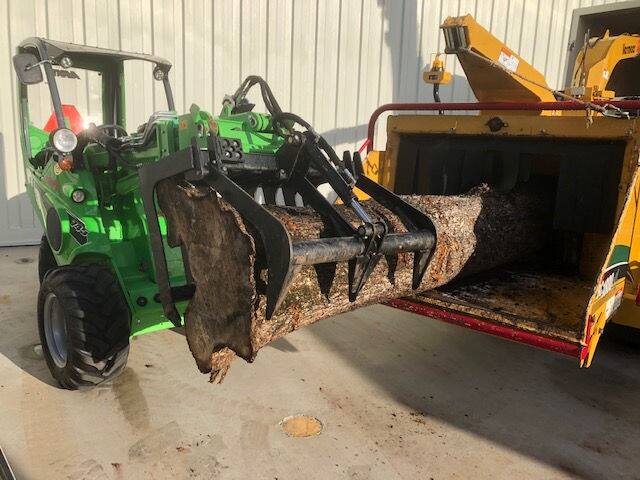 Skid steer grapple loading a large tree trunk section into a chipper